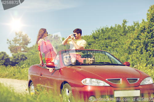 Image of happy friends with camera driving in cabriolet car