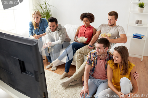 Image of happy friends with popcorn watching tv at home