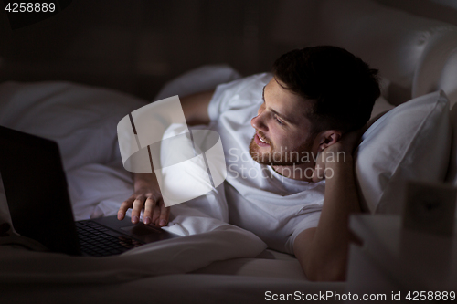 Image of happy young man with laptop in bed at home