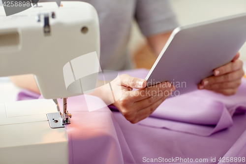 Image of tailor with sewing machine, tablet pc and fabric