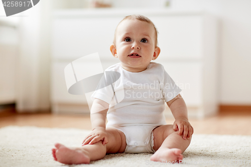 Image of happy baby boy or girl sitting on floor at home