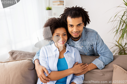 Image of happy couple sitting on sofa and hugging at home