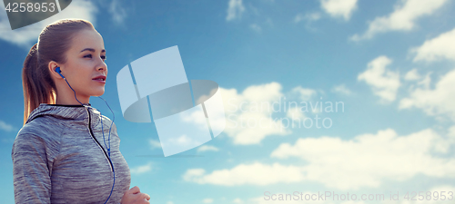 Image of happy woman with earphones running over blue sky