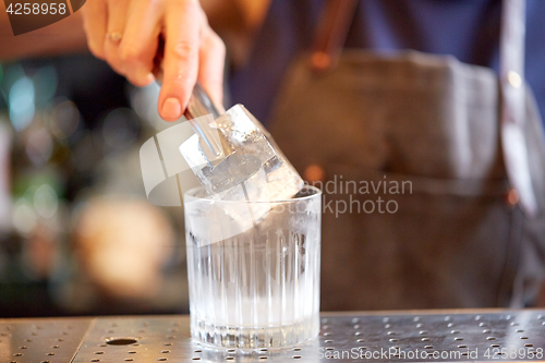 Image of bartender adding ice cube into glass at bar