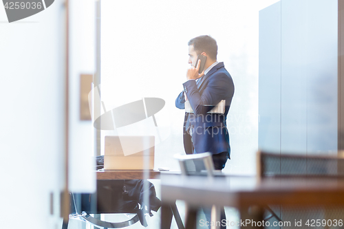 Image of Businessman talking on a mobile phone while looking through window.