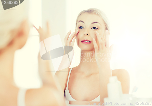 Image of happy woman applying cream to face at bathroom