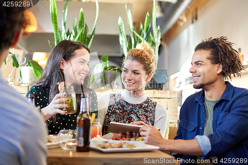 Image of friends with tablet pc, drinks and food at bar