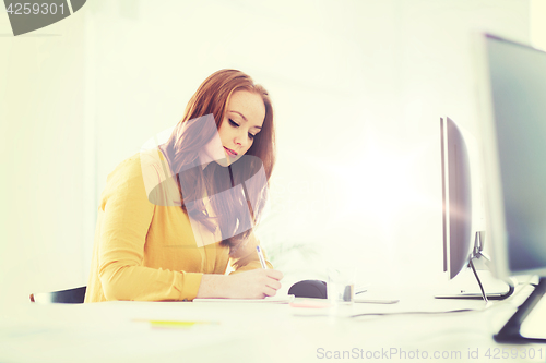 Image of creative female office worker writing to notebook