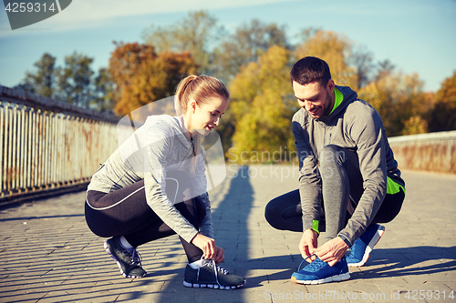 Image of smiling couple tying shoelaces outdoors