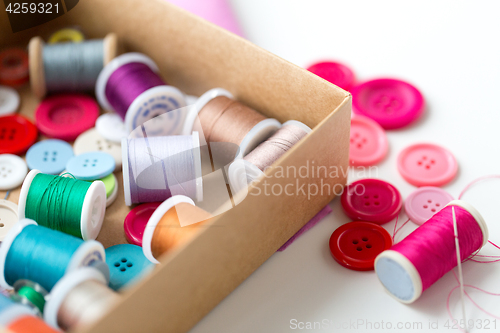 Image of box with thread spools and sewing buttons on table