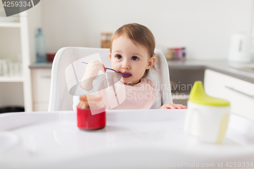 Image of baby girl with spoon eating puree from jar at home