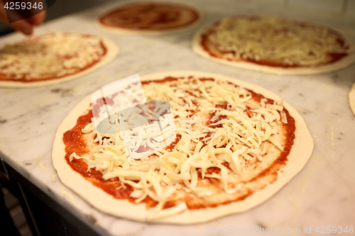 Image of raw pizza with grated cheese on table at pizzeria