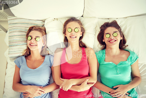 Image of happy young women with cucumber mask lying in bed