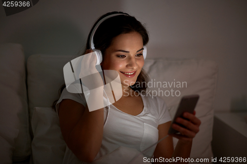 Image of woman with smartphone and headphones in bed