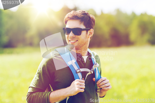 Image of happy young man with backpack hiking outdoors