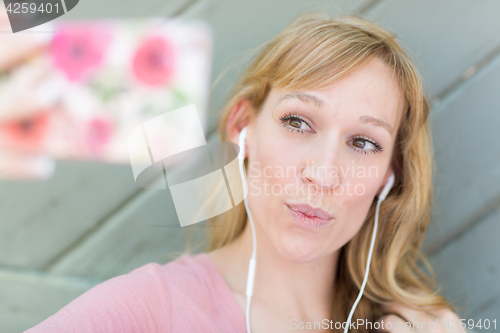 Image of Young Adult Woman Wearing Earphones Taking a Selfie with Her Sma