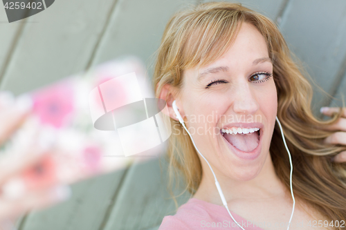 Image of Young Adult Woman Wearing Earphones Taking a Selfie with Her Sma
