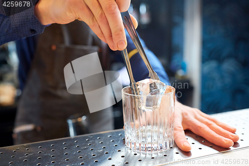 Image of bartender adding ice cube into glass at bar