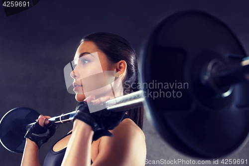 Image of young woman flexing muscles with barbell in gym