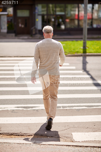 Image of senior man walking along city crosswalk