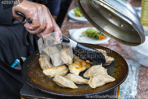 Image of Dumplings frying on grill pan on food stall.