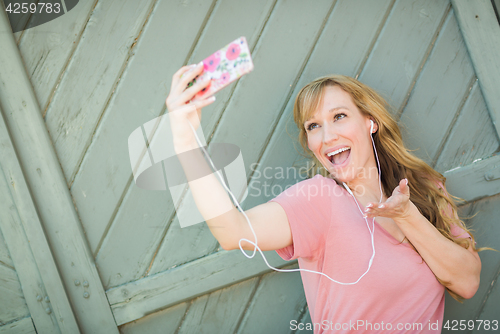 Image of Young Adult Woman Wearing Earphones Taking a Selfie with Her Sma