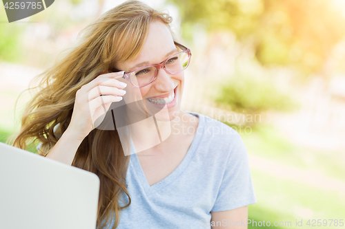 Image of Young Adult Woman Wearing Glasses Outdoors Using Her Laptop.