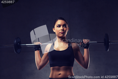 Image of young woman flexing muscles with barbell in gym