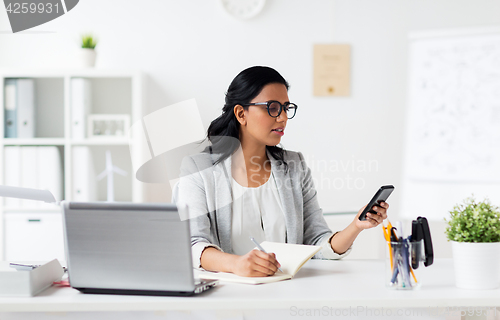 Image of businesswoman with smartphone and laptop at office