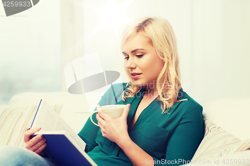 Image of  young woman with tea cup reading book at home