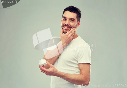 Image of happy young man applying cream to face over gray