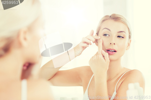 Image of woman squeezing pimple at bathroom mirror