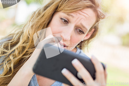 Image of Concerned Young Woman Outdoors Looking At Her Smart Phone.