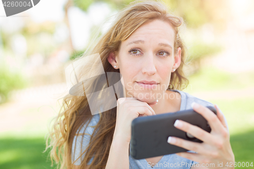 Image of Concerned Young Woman Outdoors Looking At Her Smart Phone.