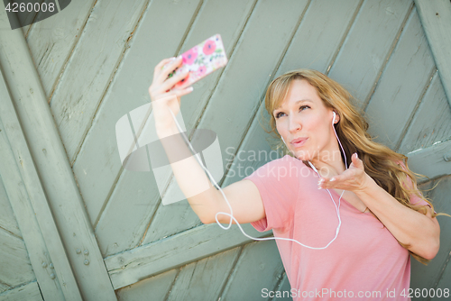Image of Young Adult Woman Wearing Earphones Taking a Selfie with Her Sma