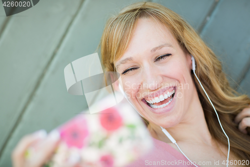 Image of Young Adult Woman Wearing Earphones Taking a Selfie with Her Sma