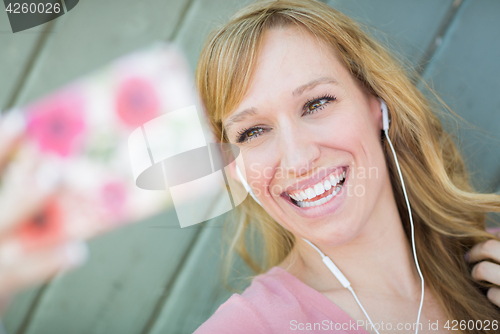 Image of Young Adult Woman Wearing Earphones Taking a Selfie with Her Sma