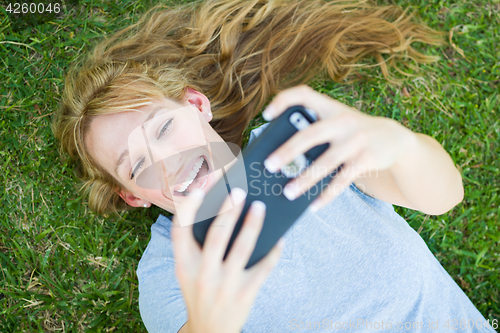 Image of Young Adult Woman Laying in Grass Taking a Selfie with Her Smart