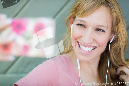 Image of Young Adult Woman Wearing Earphones Taking a Selfie with Her Sma