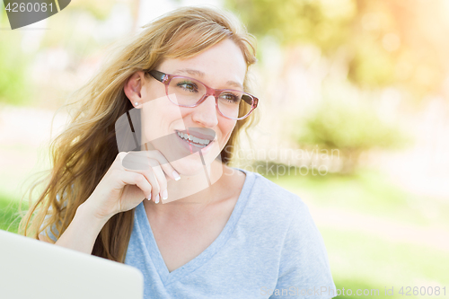 Image of Young Adult Woman Wearing Glasses Outdoors Using Her Laptop.