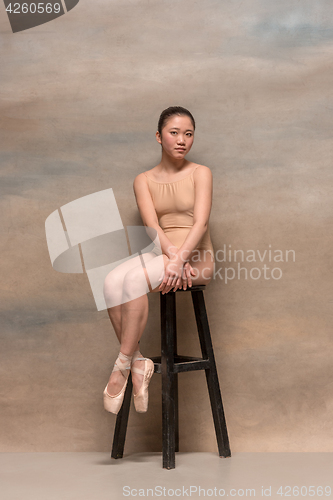 Image of Tired ballet dancer sitting on the wooden chair on a pink background