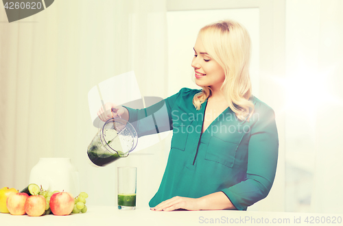 Image of happy woman with blender jug pouring juice at home