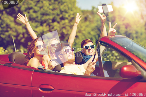 Image of friends driving in cabriolet car and taking selfie