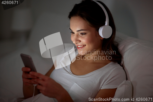 Image of woman with smartphone and headphones in bed