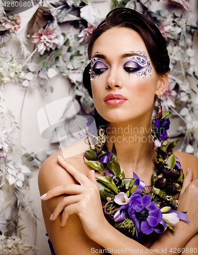 Image of floral face art with anemone in jewelry, sensual young brunette woman in studio close up