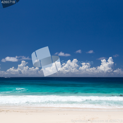 Image of Tropical beach with white sand, emerald water, blue sky with clouds.