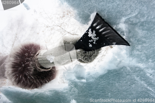 Image of hand with scraper cleaning window of car from the snow