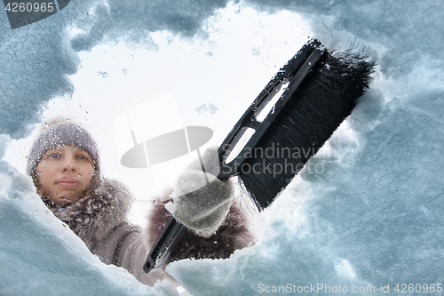 Image of woman cleaning window of car from the snow with a brush