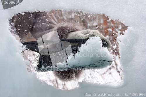 Image of hand with brush cleaning window of car from the snow, closeup