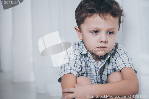 Image of Portrait of sad little boy sitting near the window